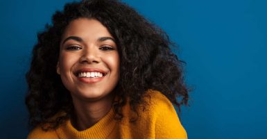 Photo of a beautiful smiling optimistic young african woman posing isolated over blue wall background.