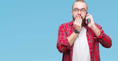 Young caucasian hipster man talking on smartphone over isolated background cover mouth with hand shocked with shame for mistake, expression of fear, scared in silence, secret concept