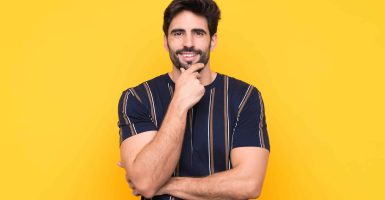 Young handsome man with beard over isolated yellow background laughing