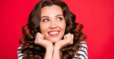 Close up portrait of adorable attractive she her girl toothy smiles arms under face looking up making wish as star fell wearing white sweater outfit isolated on red vivid bright background