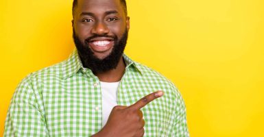 Photo of candid satisfied person toothy smile direct finger empty space proposition isolated on yellow color background.